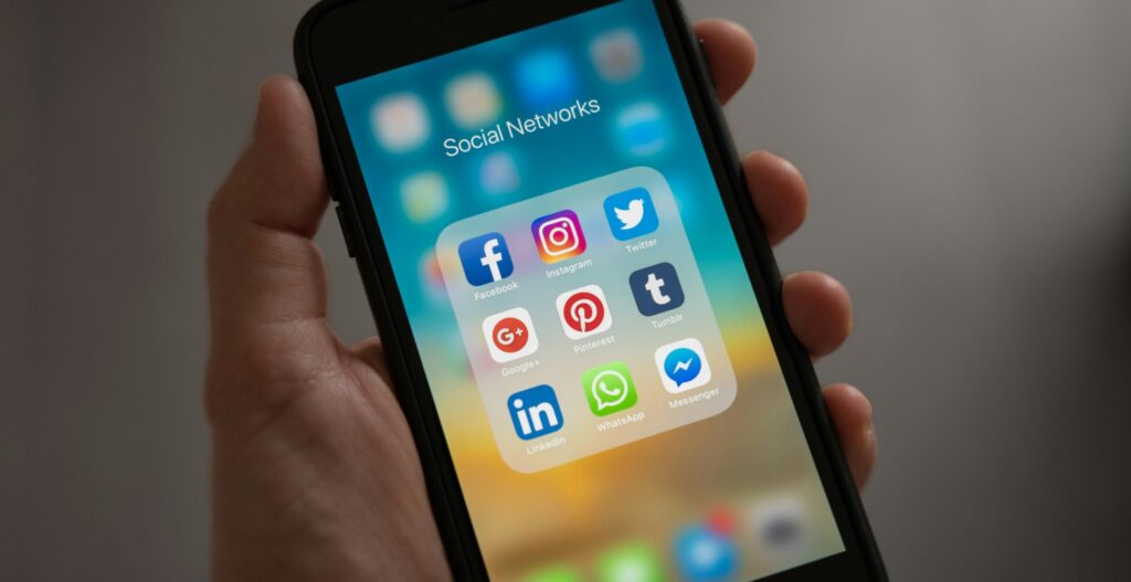 A smartphone displaying various social media icons held in a hand, showcasing modern communication apps.