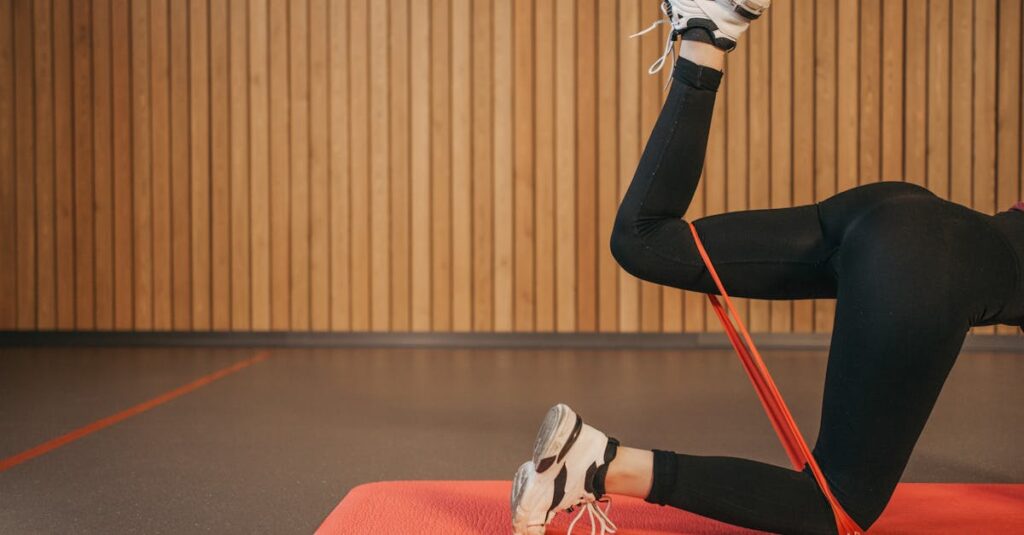 Woman in activewear working out indoors with resistance band on yoga mat, focusing on legs.