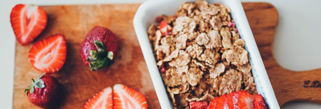 Delicious granola served with fresh strawberries on a wooden chopping board.