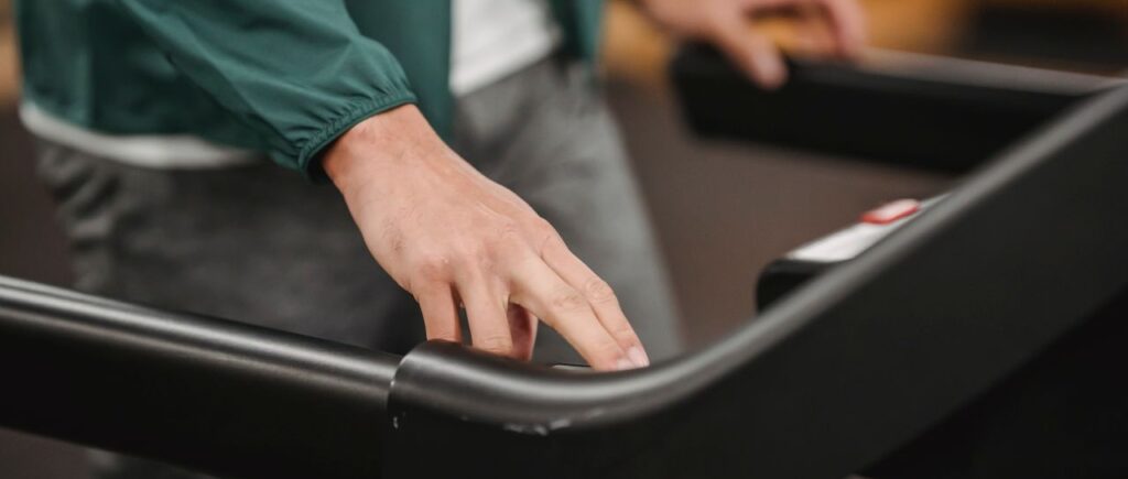 Crop anonymous male in activewear checking speed and time of treadmill on blurred background