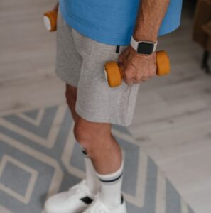 A senior adult holding dumbbells while exercising indoors, promoting a healthy lifestyle.